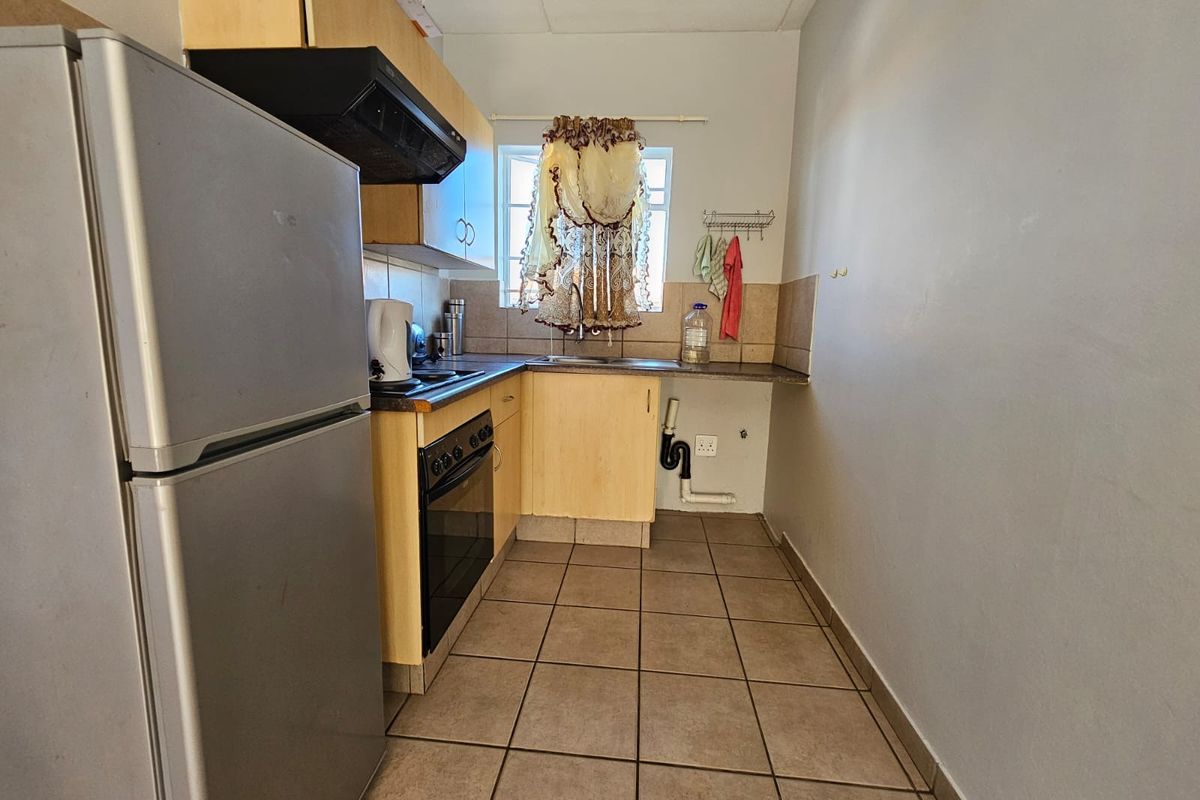 A compact kitchen featuring laminate cabinetry, a built-in oven with extractor fan, tiled flooring, and a tiled backsplash.