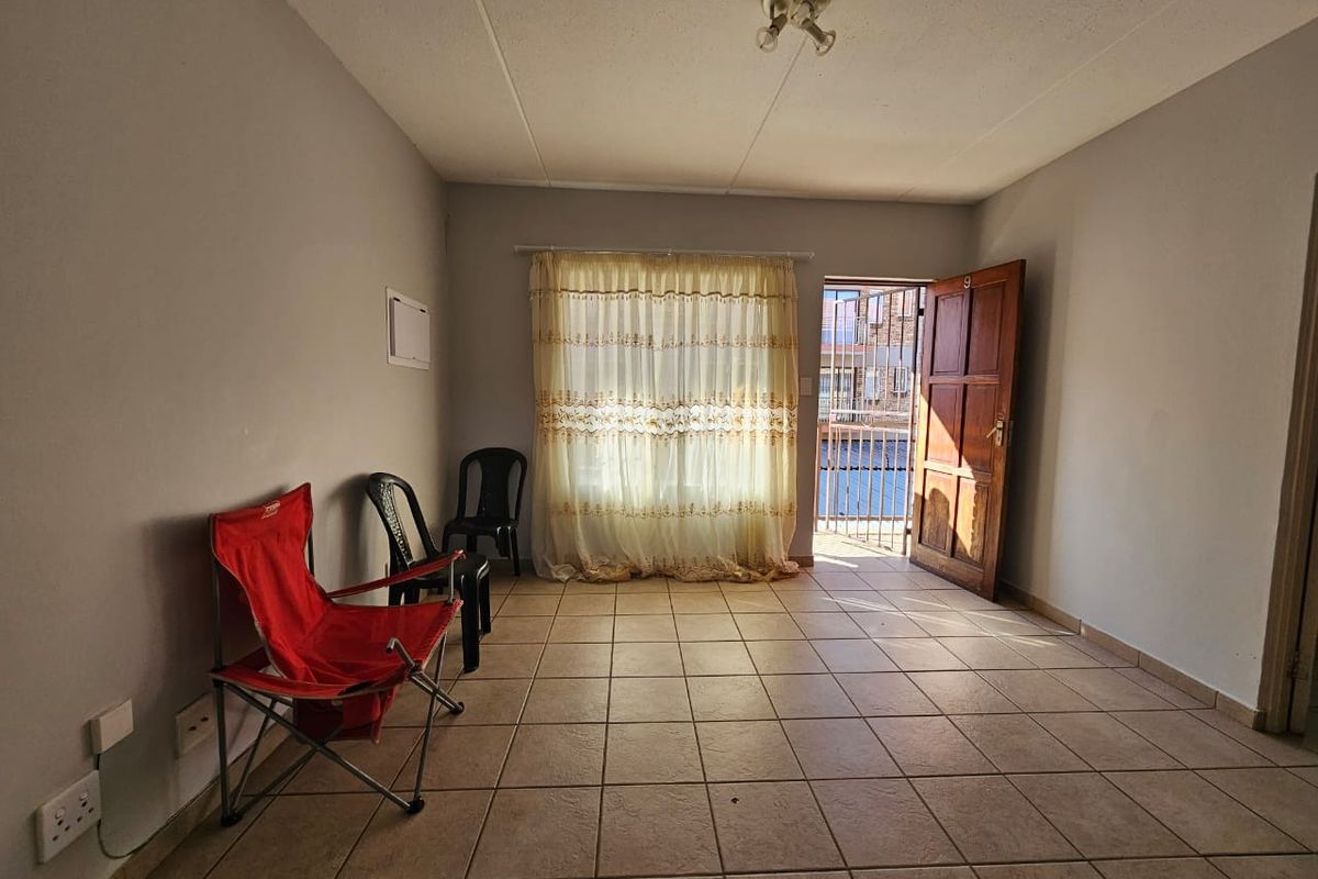A vacant living room featuring tiled flooring, a timber entrance door with security gate, and neutral wall finishes, offering a blank canvas for renovation.
