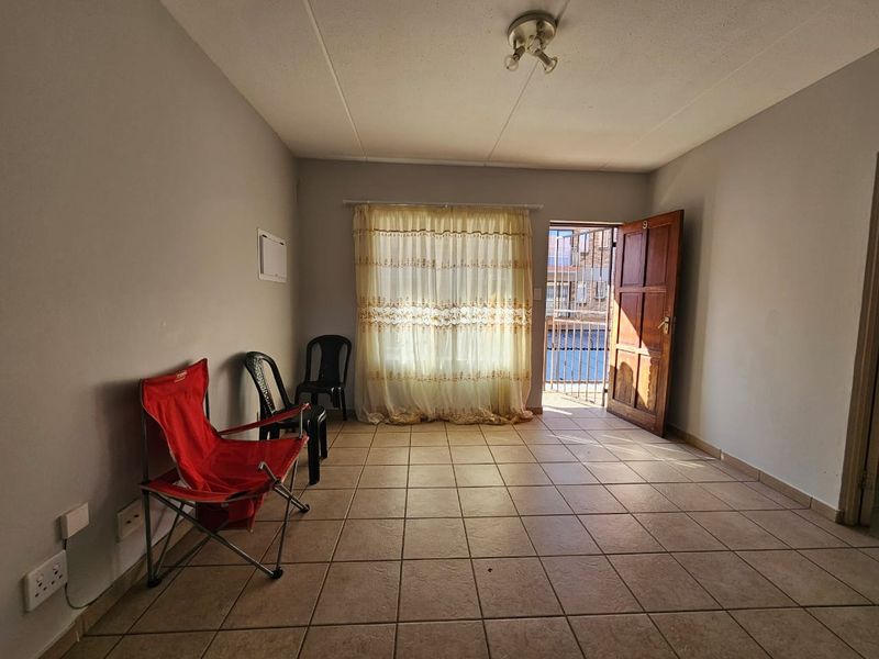 A vacant living room featuring tiled flooring, a timber entrance door with security gate, and neutral wall finishes, offering a blank canvas for renovation.