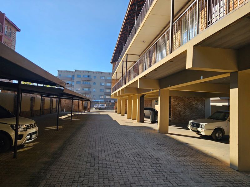 Exterior view of an apartment complex featuring covered parking bays, brick paving, and multi-level balconies with metal railings.