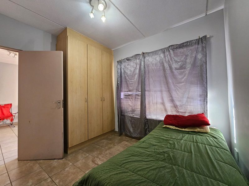 A bedroom featuring tiled flooring, a built-in wardrobe, and a ceiling light fixture. The room requires cosmetic updates to improve its overall condition.