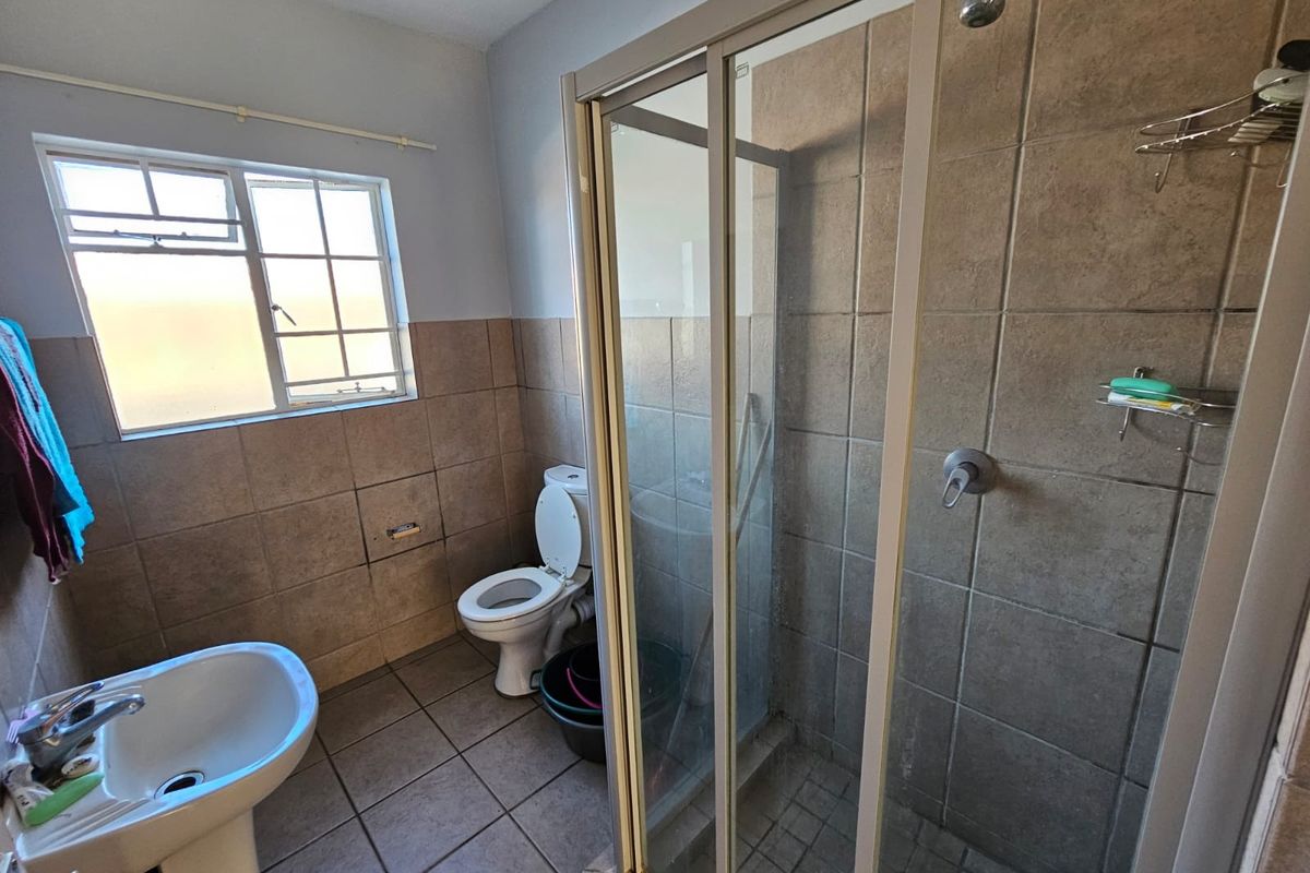 A functional bathroom featuring a pedestal basin, toilet, and a glass-enclosed shower with tiled walls and flooring.