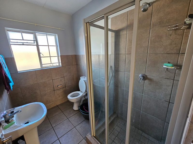 A functional bathroom featuring a pedestal basin, toilet, and a glass-enclosed shower with tiled walls and flooring.