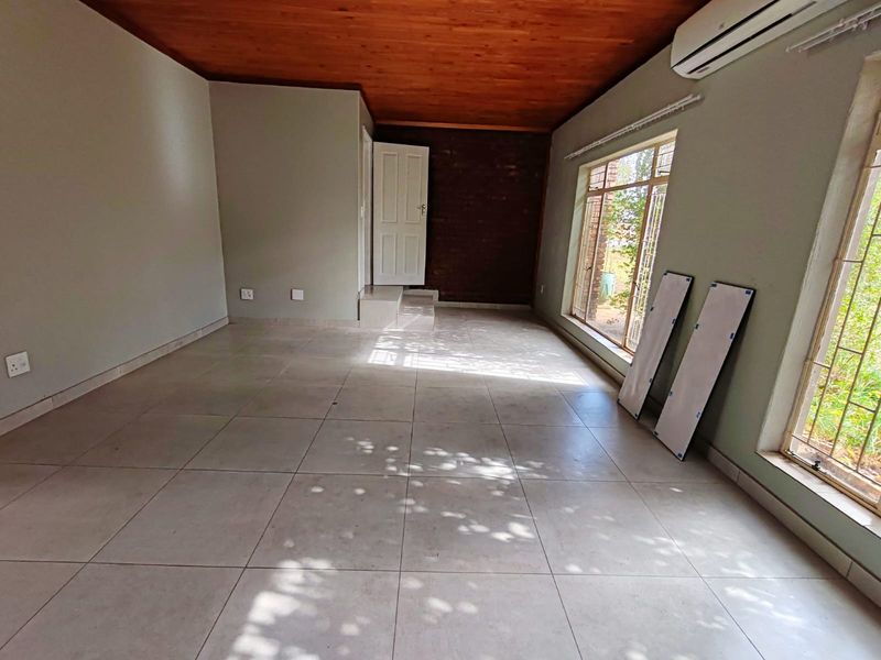 Spacious living area featuring tiled flooring, a warm timber ceiling, an exposed brick accent wall, and a wall-mounted air conditioning unit.