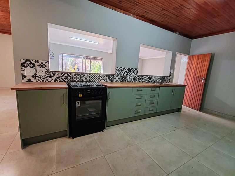 A functional kitchen featuring sage green cabinetry, wooden countertops, a patterned tile backsplash, and a timber ceiling, with convenient pass-through windows to adjacent living areas.