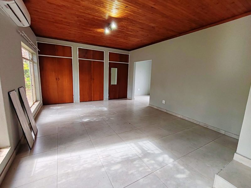 Spacious bedroom featuring tiled flooring, built-in wooden cupboards, and a warm timber ceiling, offering a clean and versatile living space.