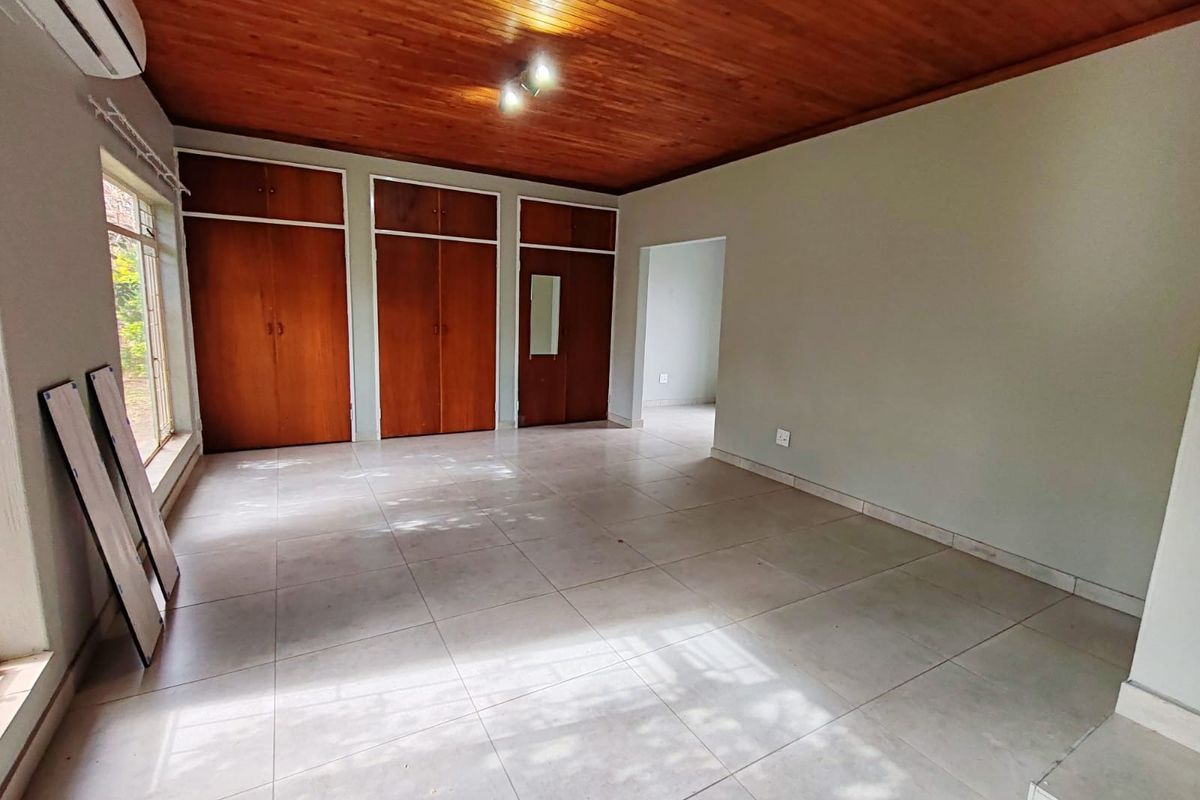 Spacious bedroom featuring tiled flooring, built-in wooden cupboards, and a warm timber ceiling, offering a clean and versatile living space.