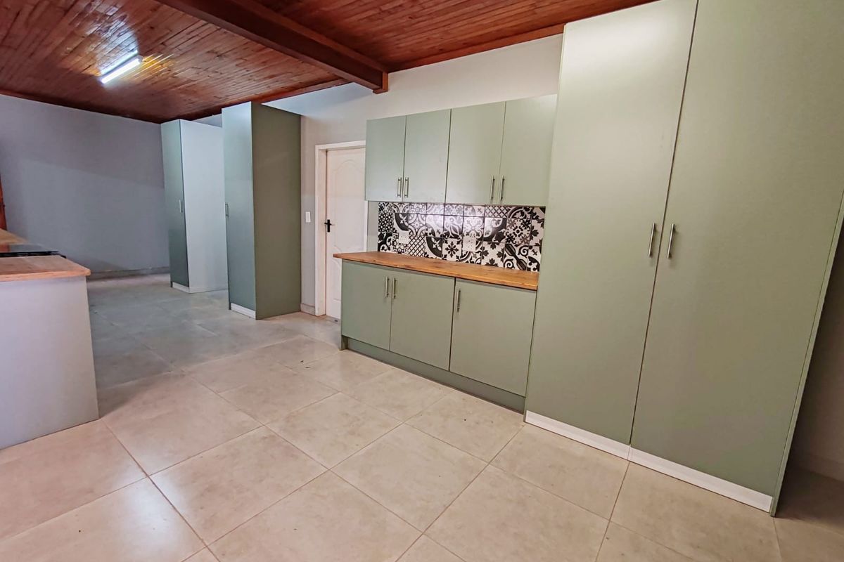 A modern kitchen featuring sage green cabinetry, wooden countertops, a decorative patterned tile backsplash, and a warm exposed timber ceiling.
