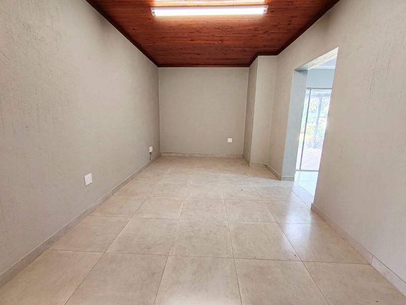 An empty living area featuring neutral tiled flooring and a warm timber tongue and groove ceiling with direct access to an outdoor space.