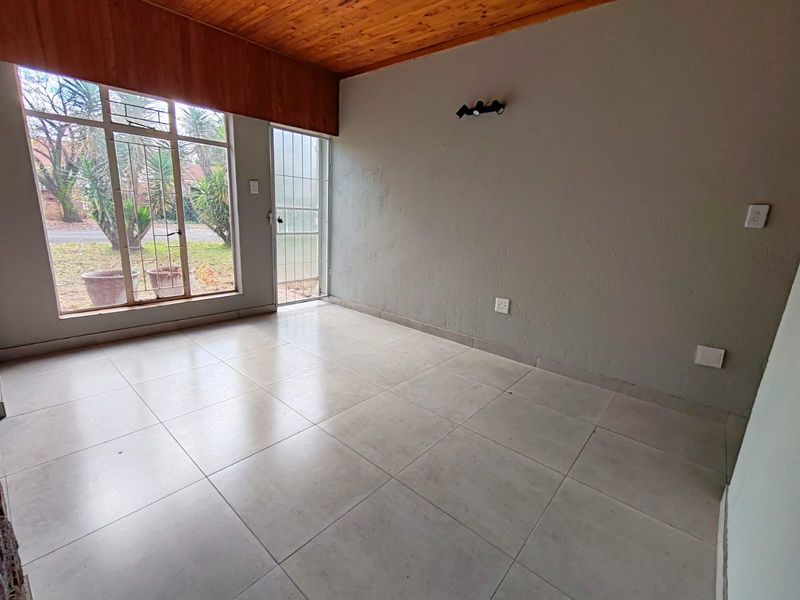 An empty living room featuring tiled flooring, a timber-paneled ceiling, and large windows with security bars, offering a bright and versatile living space.