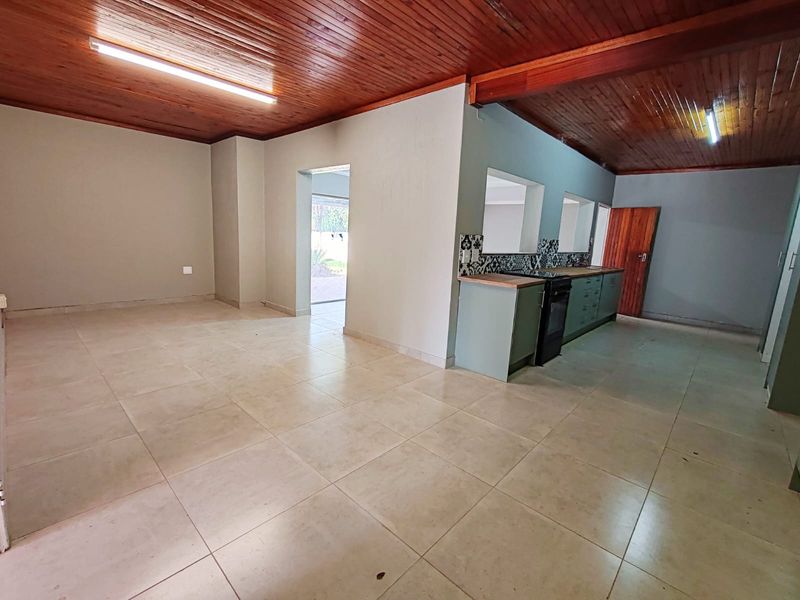 Spacious open-plan living and kitchen area featuring timber ceilings, tiled floors, and built-in cabinetry with a modern tiled backsplash.