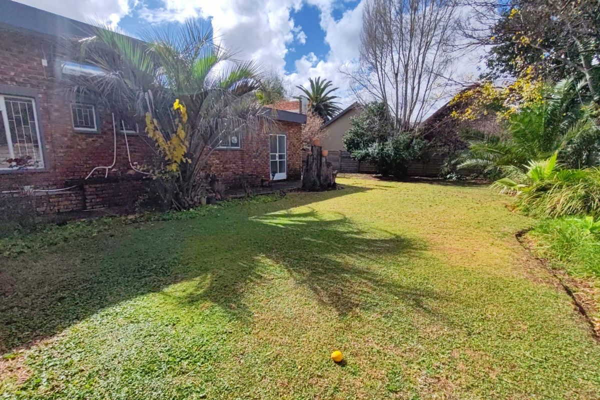 A rear garden view featuring a brick exterior facade, established trees, and a lawn area.