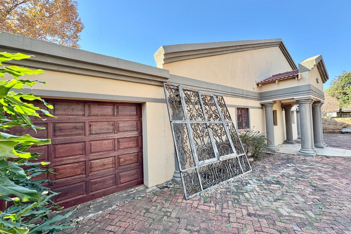 Front exterior view of the property featuring a garage, brick paved driveway, and decorative concrete columns under a clear blue sky.