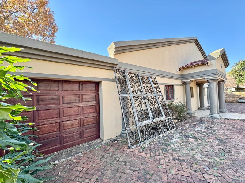 Front exterior view of the property featuring a garage, brick paved driveway, and decorative concrete columns under a clear blue sky.