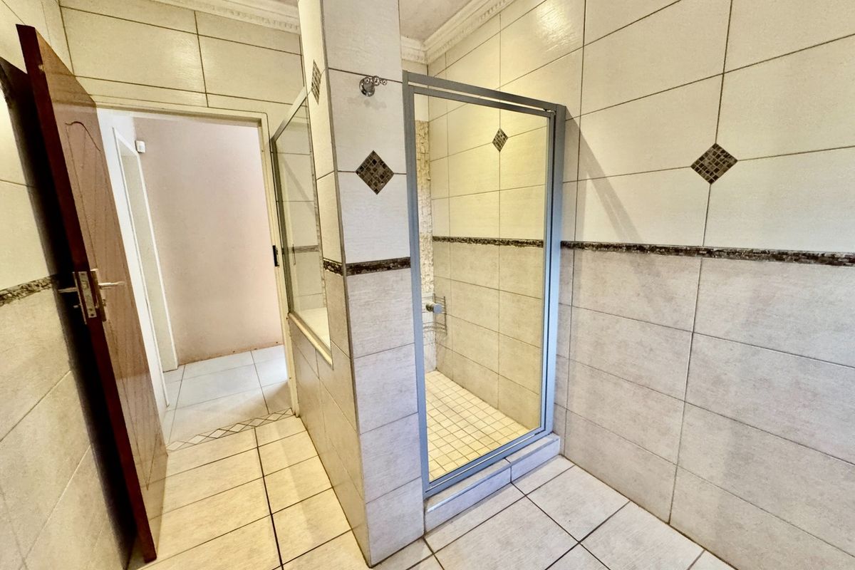 A tiled bathroom featuring a walk-in shower enclosure with a glass door and neutral wall tiling.