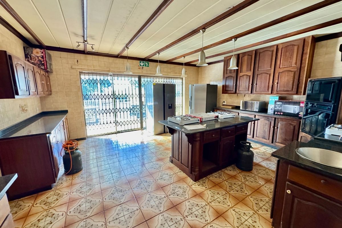 Spacious kitchen featuring wooden cabinetry, granite countertops, a central island with a gas hob, and direct access to the outdoor area via a security gate.