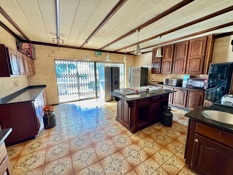 Spacious kitchen featuring wooden cabinetry, granite countertops, a central island with a gas hob, and direct access to the outdoor area via a security gate.
