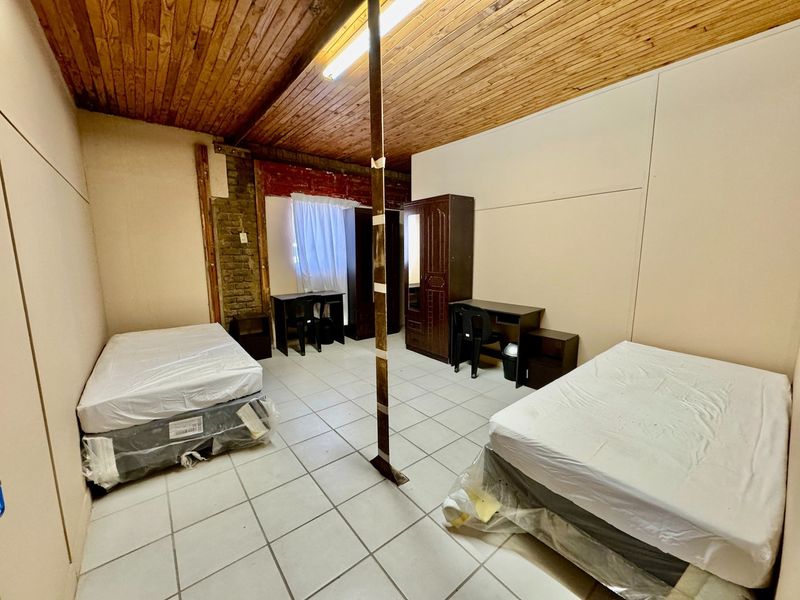 A bedroom featuring tiled flooring, a timber ceiling, and an exposed brick wall section, currently configured with two beds.
