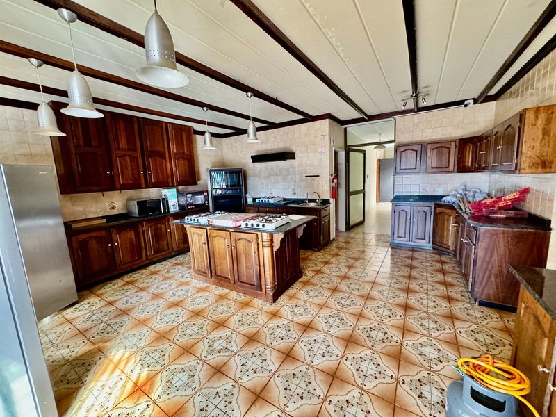 Spacious kitchen featuring extensive wooden cabinetry, granite countertops, a central island with a gas hob, and exposed ceiling beams.