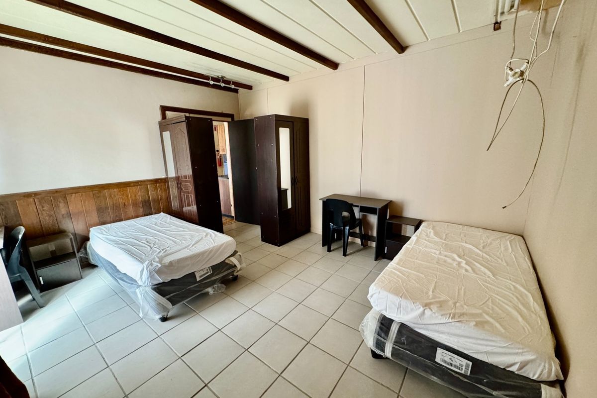 A bedroom featuring tiled flooring, wood paneling, and exposed ceiling beams, currently requiring maintenance to address exposed wiring and wall finishes.