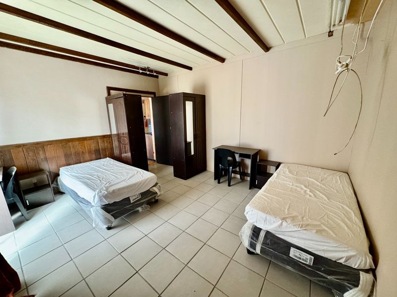 A bedroom featuring tiled flooring, wood paneling, and exposed ceiling beams, currently requiring maintenance to address exposed wiring and wall finishes.
