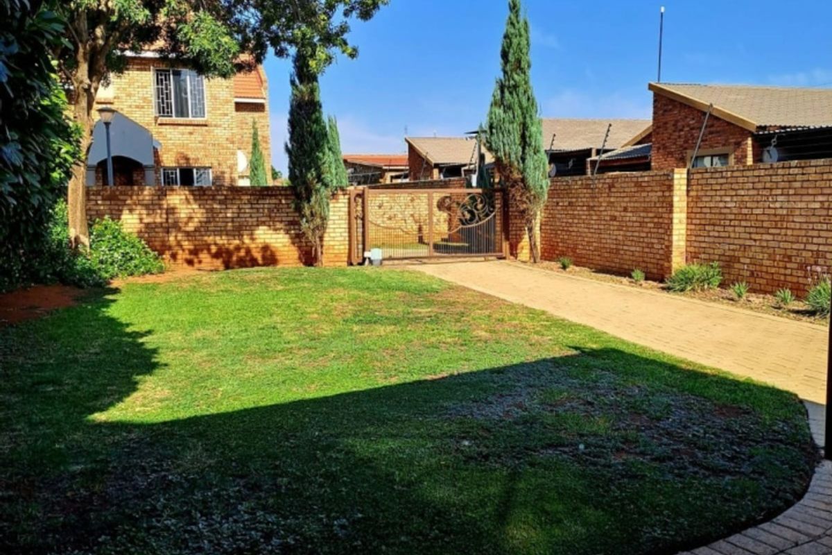 A private rear garden featuring a well-maintained lawn, paved driveway, and secure brick boundary walls with a metal gate.