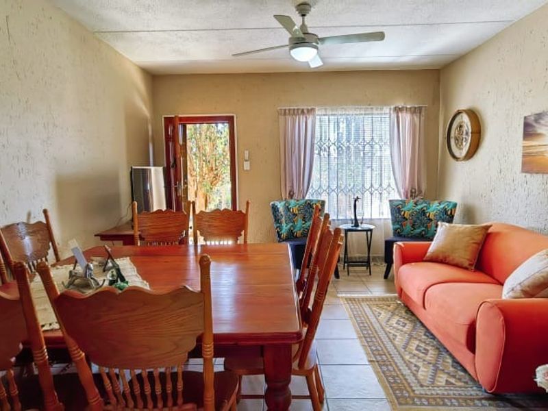Open-plan living and dining area featuring tiled flooring, a ceiling fan, and direct access to the exterior through a security gate.