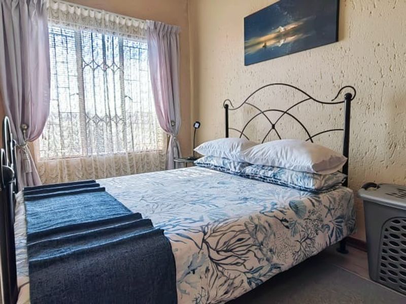 A cozy bedroom featuring textured walls, laminate flooring, and a window fitted with a security gate.