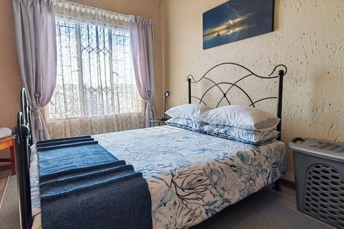 A cozy bedroom featuring textured walls, laminate flooring, and a window fitted with a security gate.