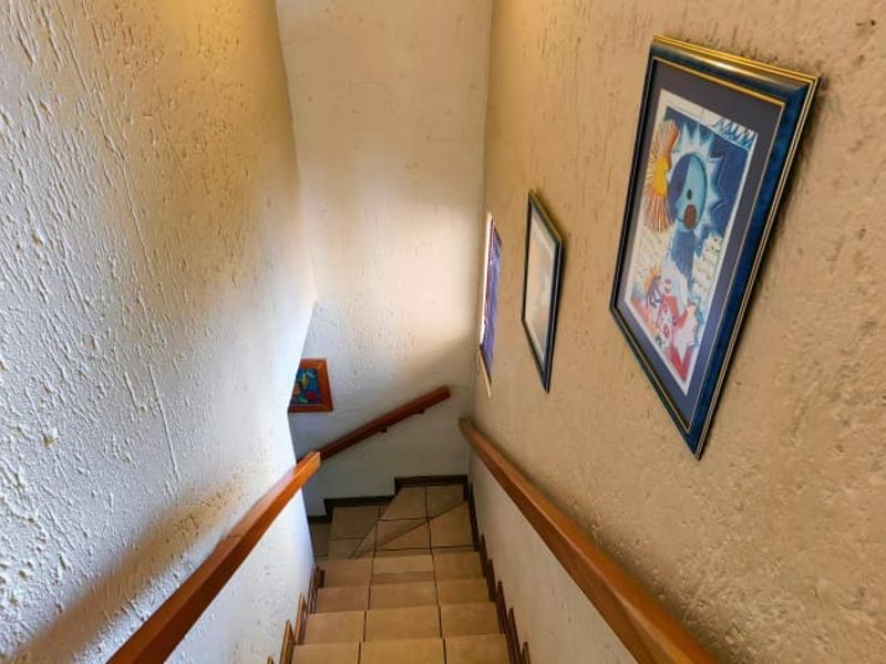 A staircase featuring tiled steps, a wooden handrail, and textured wall finishes, providing access between levels in the townhouse.