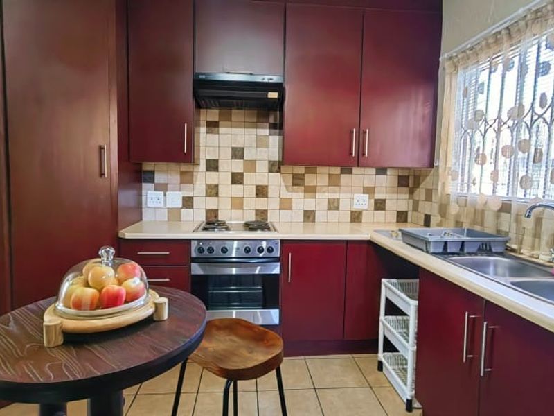 A functional kitchen featuring dark wood-finish cabinetry, a gas hob with extractor, double basin sink, and tiled backsplash with neutral floor tiles.