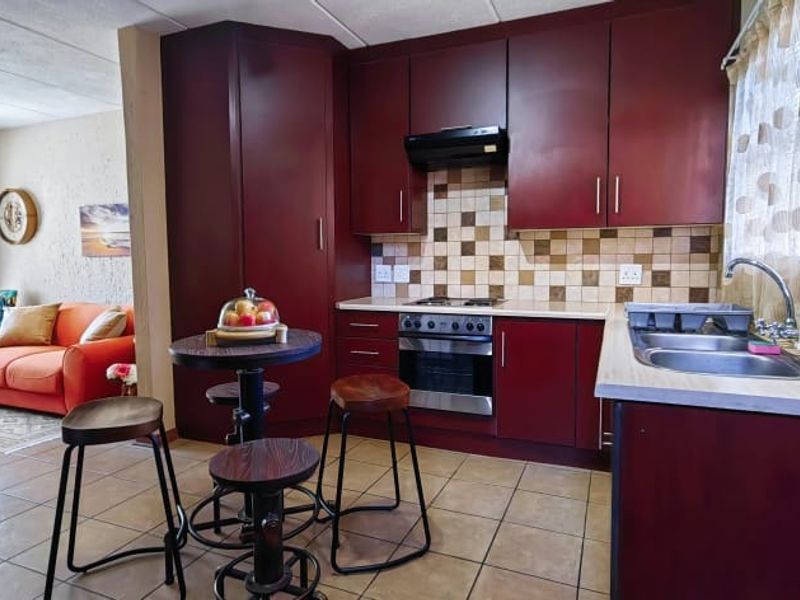 Open-plan kitchen and living area featuring dark wood cabinetry, tiled backsplash, built-in oven, and tiled flooring throughout the space.