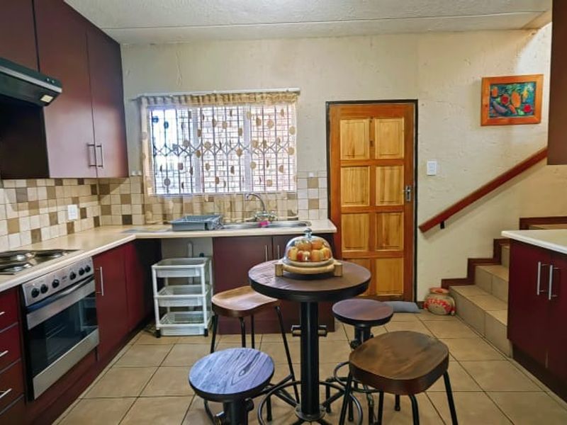 A functional kitchen featuring dark wood cabinetry, tiled backsplash, built-in oven and hob, and direct access to the staircase and exterior door.