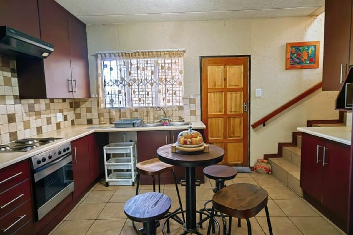 A functional kitchen featuring dark wood cabinetry, tiled backsplash, built-in oven and hob, and direct access to the staircase and exterior door.