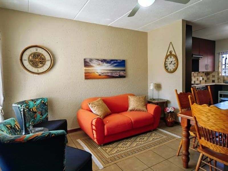 Open-plan living and dining area featuring tiled floors, a ceiling fan, and an adjoining kitchen with built-in cabinetry and tiled backsplash.