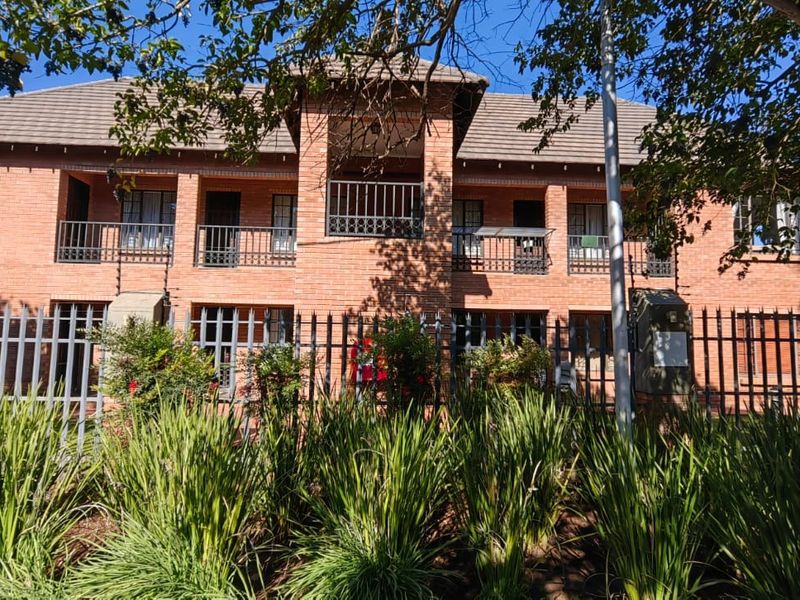 Front elevation of the Varsity Villa apartment complex, featuring a classic face brick facade, tiled roof, and secure metal perimeter fencing.