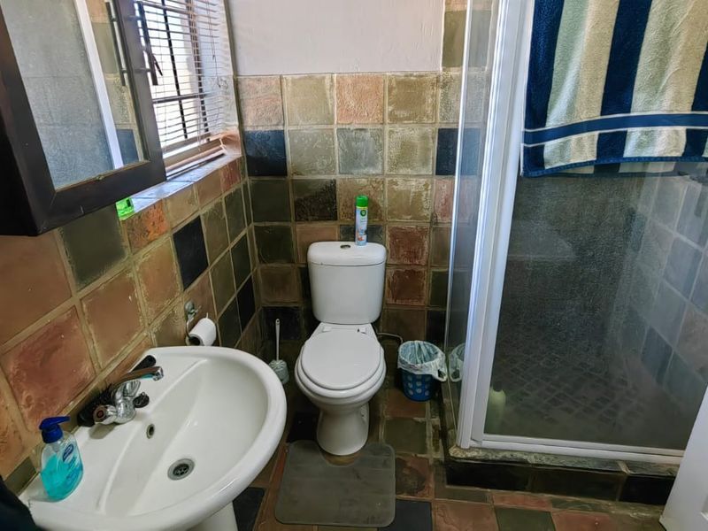 A functional bathroom featuring a pedestal basin, toilet, and a glass-enclosed shower with dated multi-colored wall and floor tiles.