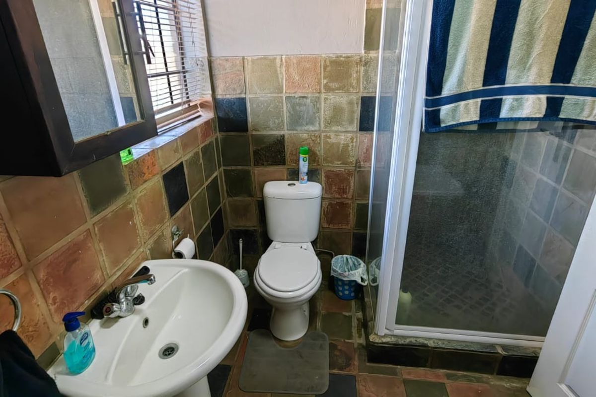 A functional bathroom featuring a pedestal basin, toilet, and a glass-enclosed shower with dated multi-colored wall and floor tiles.