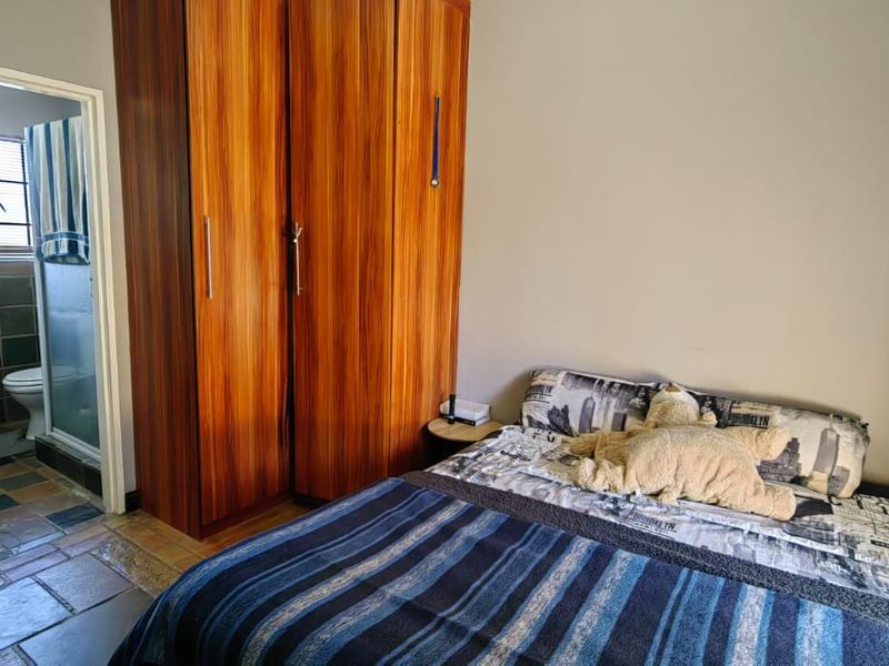 A bedroom featuring a built-in wooden wardrobe and direct access to an en-suite bathroom with tiled flooring.