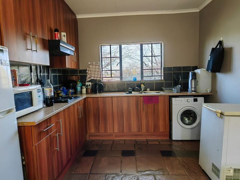 Functional kitchen featuring wood-look laminate cabinetry, tiled backsplash, and integrated sink area with space for laundry appliances.