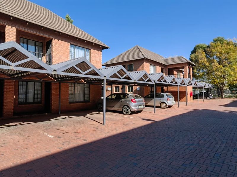 Exterior view of a brick apartment complex featuring covered parking bays and a paved driveway area.