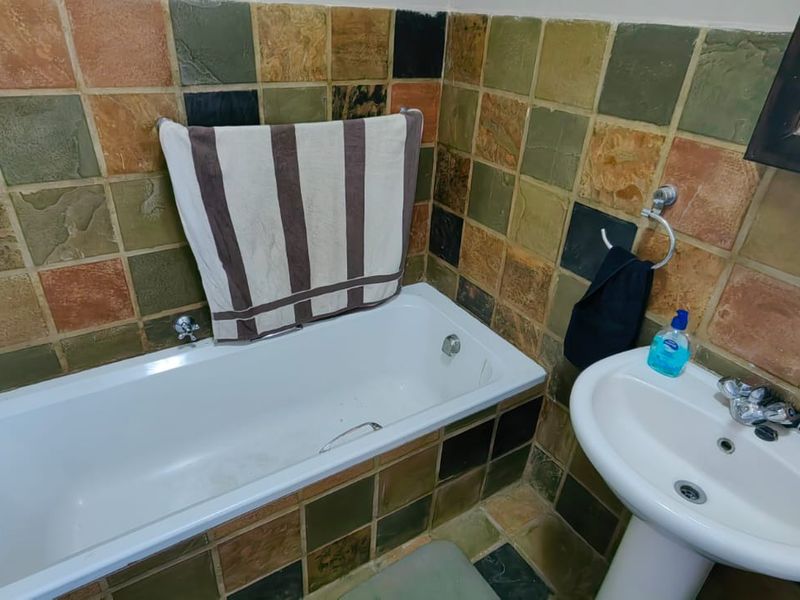 A bathroom featuring a standard bathtub and a pedestal basin, finished with multi-colored decorative wall tiles.