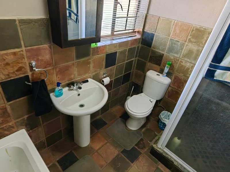 A functional bathroom featuring a pedestal basin, toilet, shower enclosure, and bathtub with dated multi-colored wall and floor tiling.
