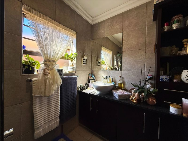 A well-maintained bathroom featuring a modern vessel sink, dark vanity cabinetry, and neutral wall tiling with a functional window for natural light.