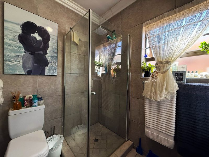 A functional bathroom featuring a glass-enclosed shower with a rain shower head, tiled walls, and a standard toilet.