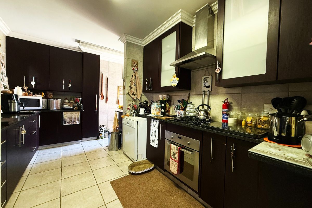 A functional kitchen featuring dark wood cabinetry, granite countertops, built-in oven, gas hob, and stainless steel extractor fan with tiled flooring.