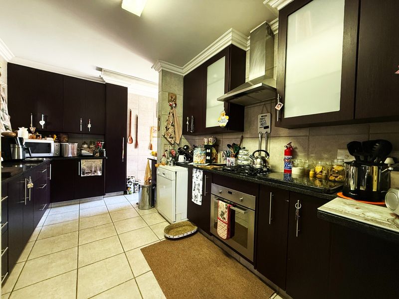 A functional kitchen featuring dark wood cabinetry, granite countertops, built-in oven, gas hob, and stainless steel extractor fan with tiled flooring.