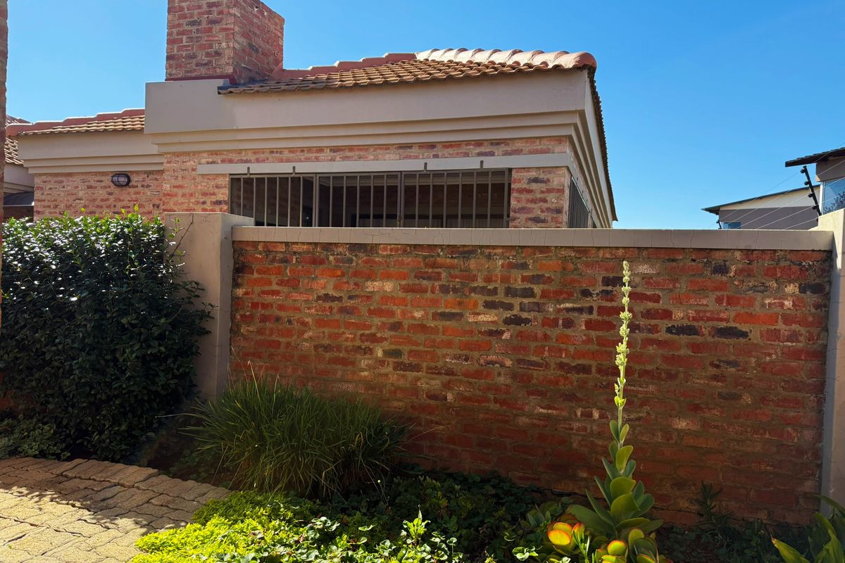 A view of the rear exterior featuring a brick boundary wall, paved walkway, and a tiled roof with a brick chimney.