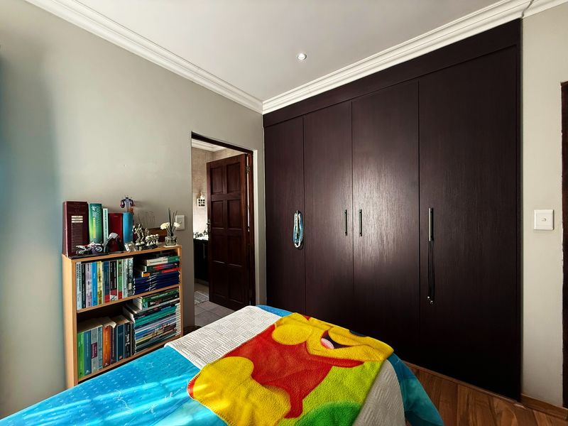 A well-maintained bedroom featuring dark wood built-in cupboards, laminate flooring, and decorative cove cornicing, with an adjoining en-suite bathroom.