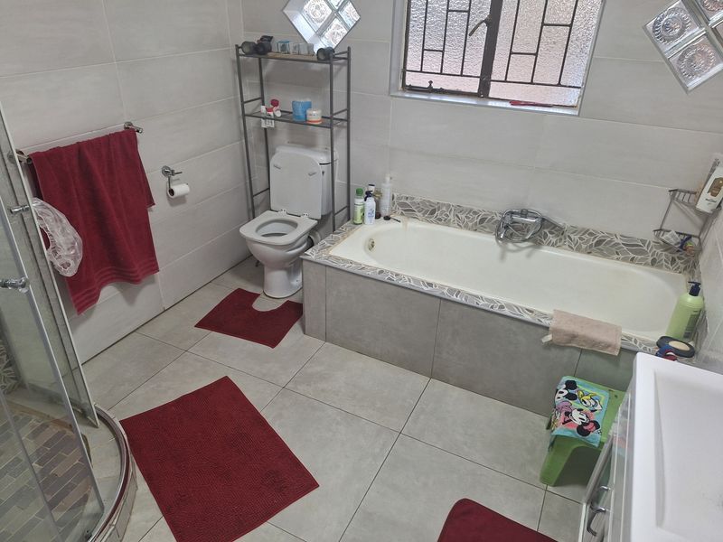 A functional bathroom featuring a built-in bathtub, separate shower enclosure, and tiled finishes throughout.